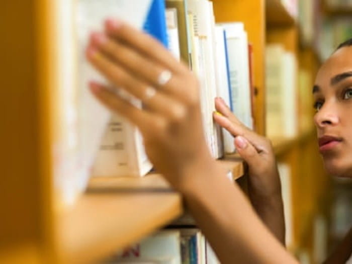 Young woman taking a book down from a library shelf