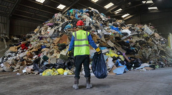 A person standing in front a huge pile of rubbish holding a bin bag