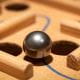 silver marble sitting on a wooden board maze game between two holes on a blue line