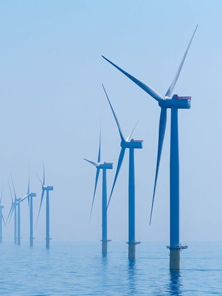 photo of a row of wind turbines standing in the blue sea water renewable energy