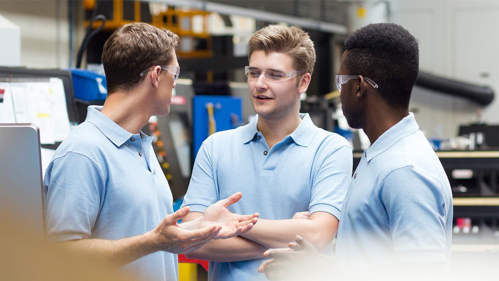 three young men apprentices apprenticeship work warehouse blue polo shirts safety glasses